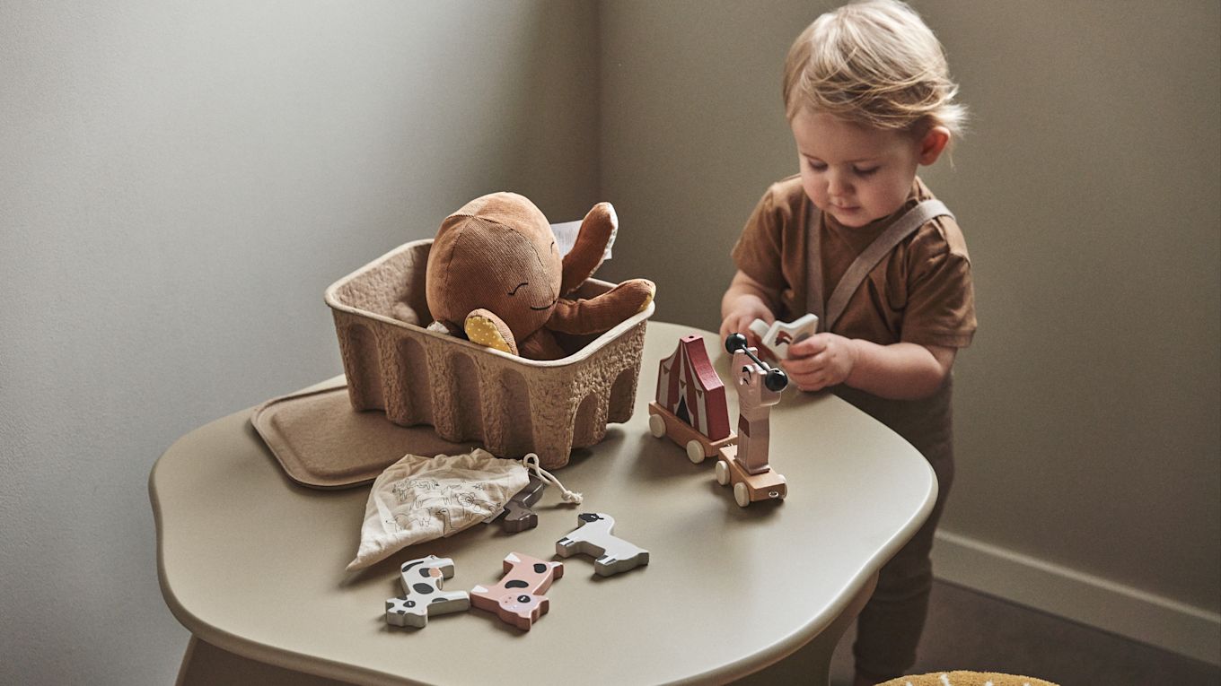 Een kind speelt met houten speelgoed uit een papieren opbergdoos - een praktisch idee voor de kinderkamer. 