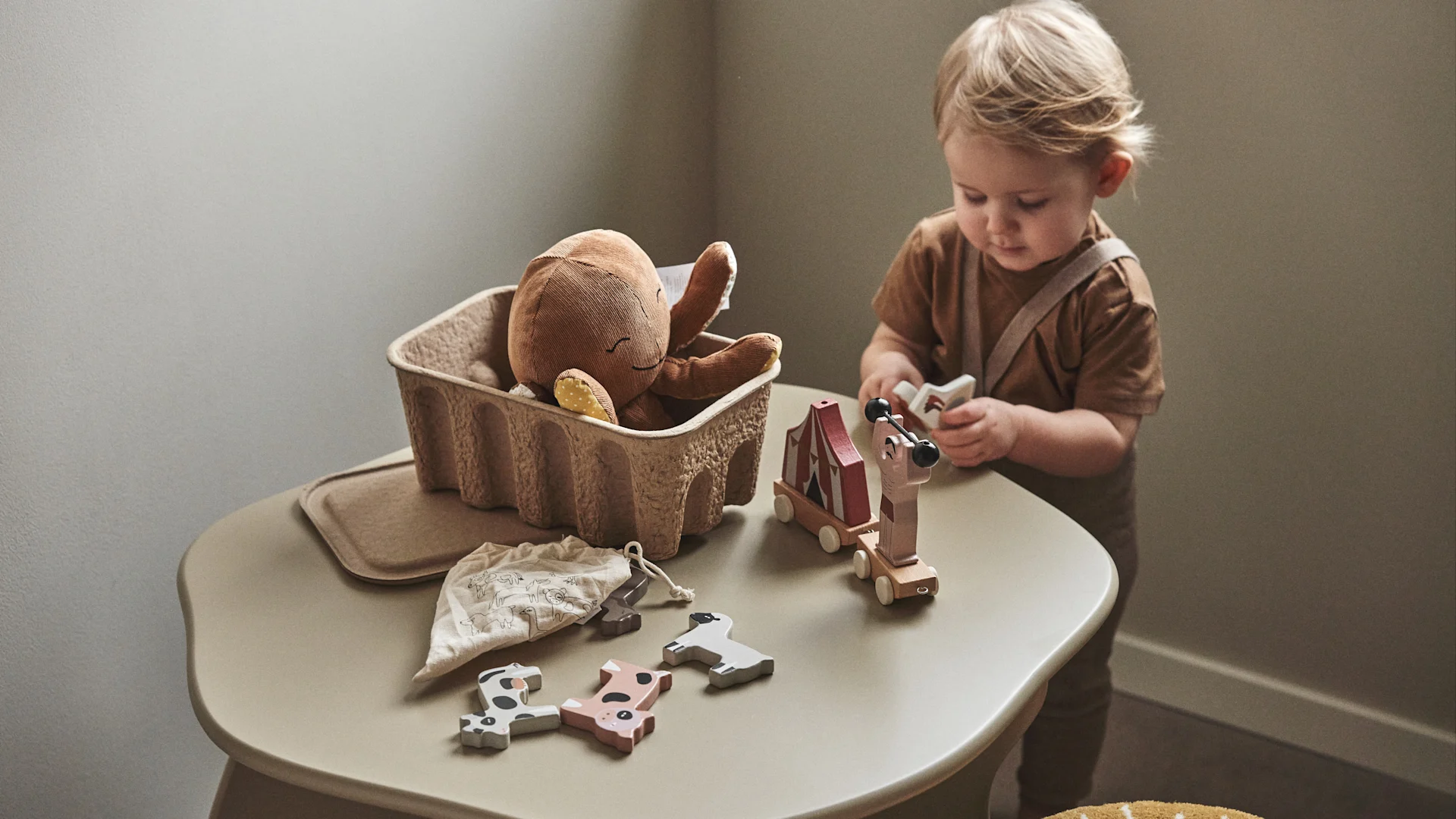 Een kind speelt met houten speelgoed uit een papieren opbergdoos - een praktisch idee voor de kinderkamer.