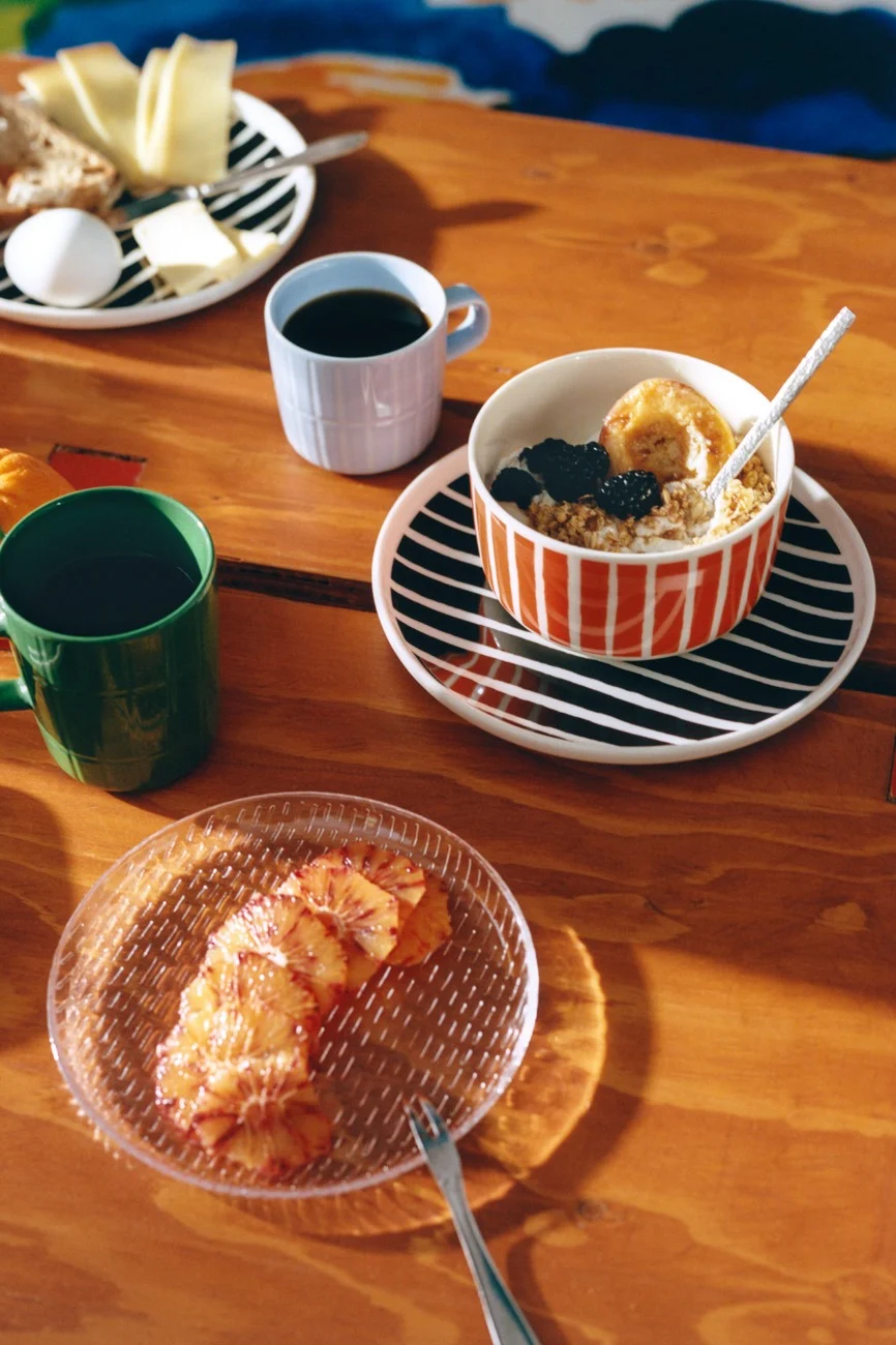 Ontbijt op houten tafel met gestreepte borden, koffie, havermout, kaas, brood, ei en bloedsinaasappelplakjes.