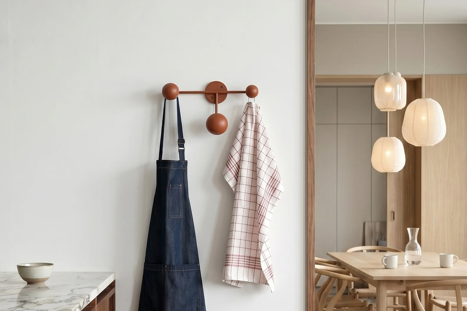Keuken met marmer. Blauw schort, geruite handdoek aan rek. Eetkamer met tafel en hanglampen.