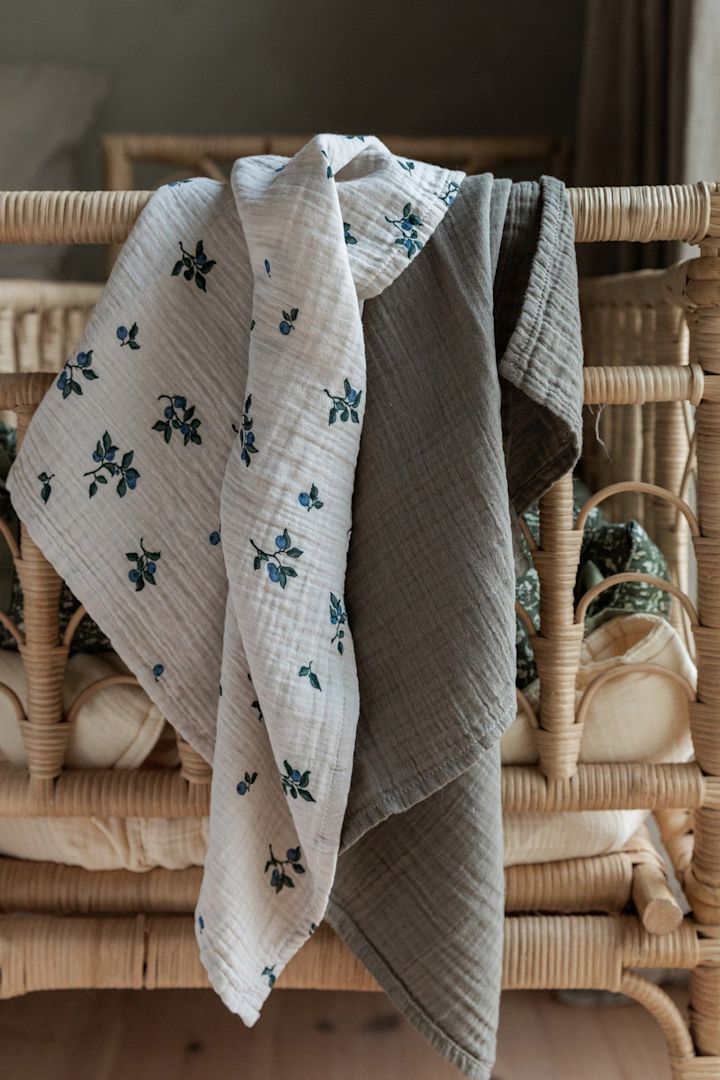 De Blueberry hydrofiele doeken van Garbo&Friends, die hier over een bedrand hangen, zijn niet alleen ideaal als knuffeldeken, maar ook als spuugdoek, waardoor ze een praktisch cadeau voor een babyshower zijn.