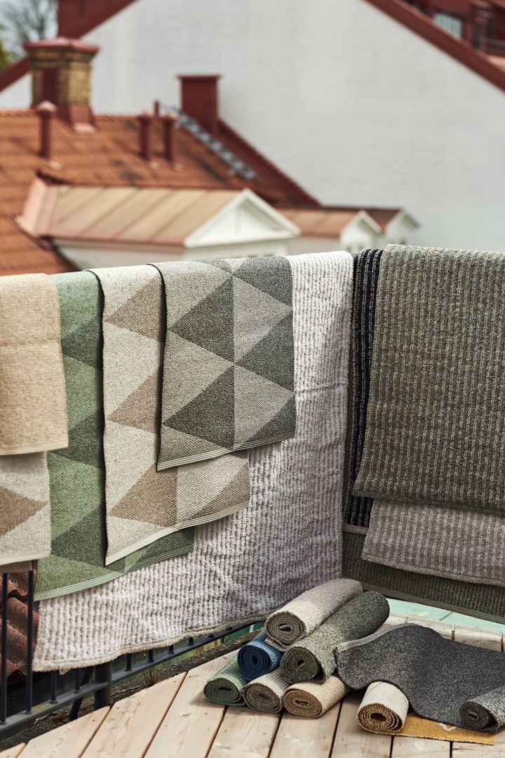 Vloerkleed voor buiten: Hier zie je de vele vloerkleden voor buiten van Scandi Living in verschillende maten, materialen en kleuren die over de reling van een balkon hangen.