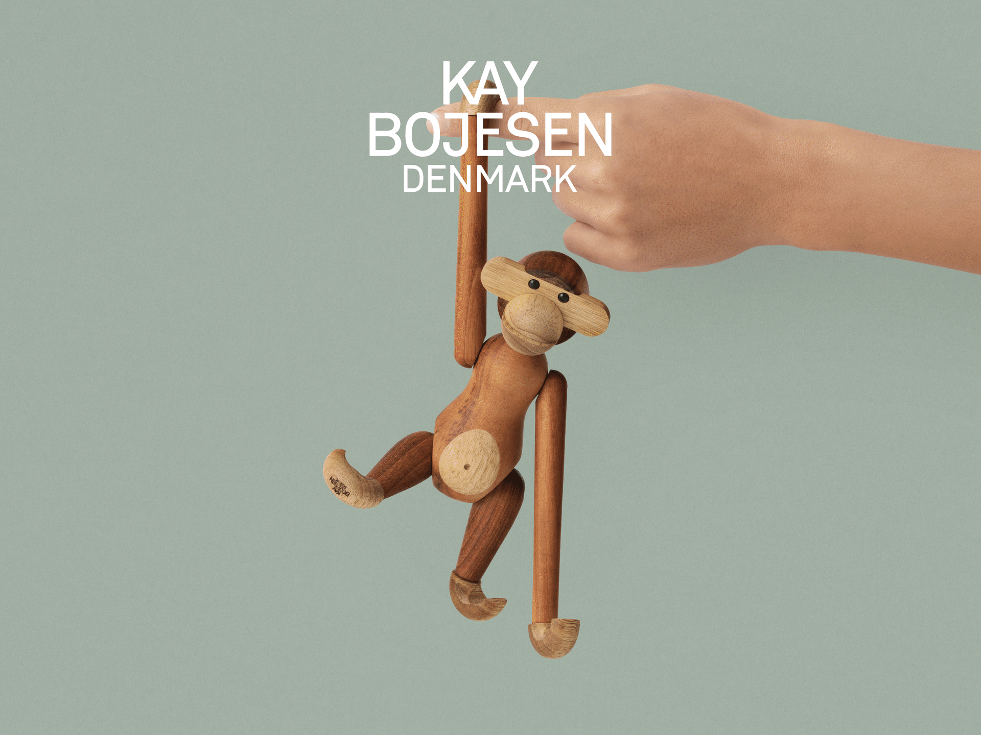 Een hand houdt een houten apenspeeltje vast, met de tekst Kay Bojesen Denmark.