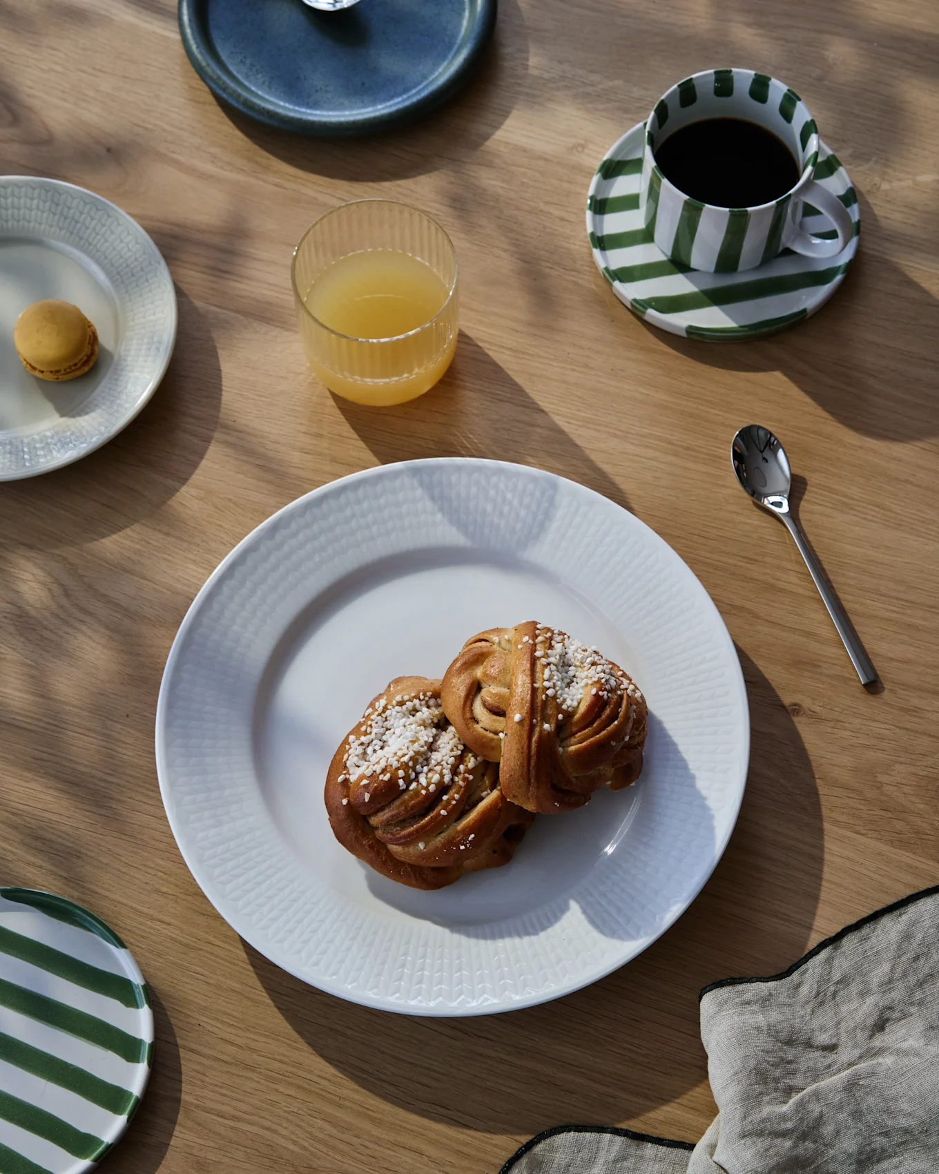 Een ontbijt op een houten tafel met twee kaneelbroodjes, koffie in een gestreepte kop, sinaasappelsap en een macaron.