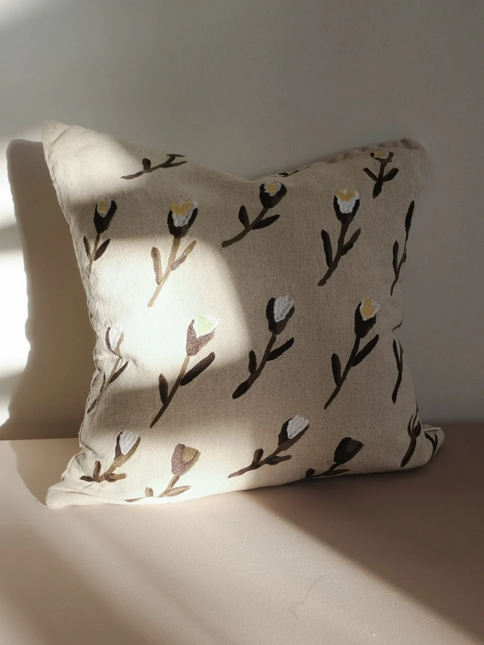 Lichtbeige kussen met een patroon van gestileerde donkerbruine en witte bloemen.