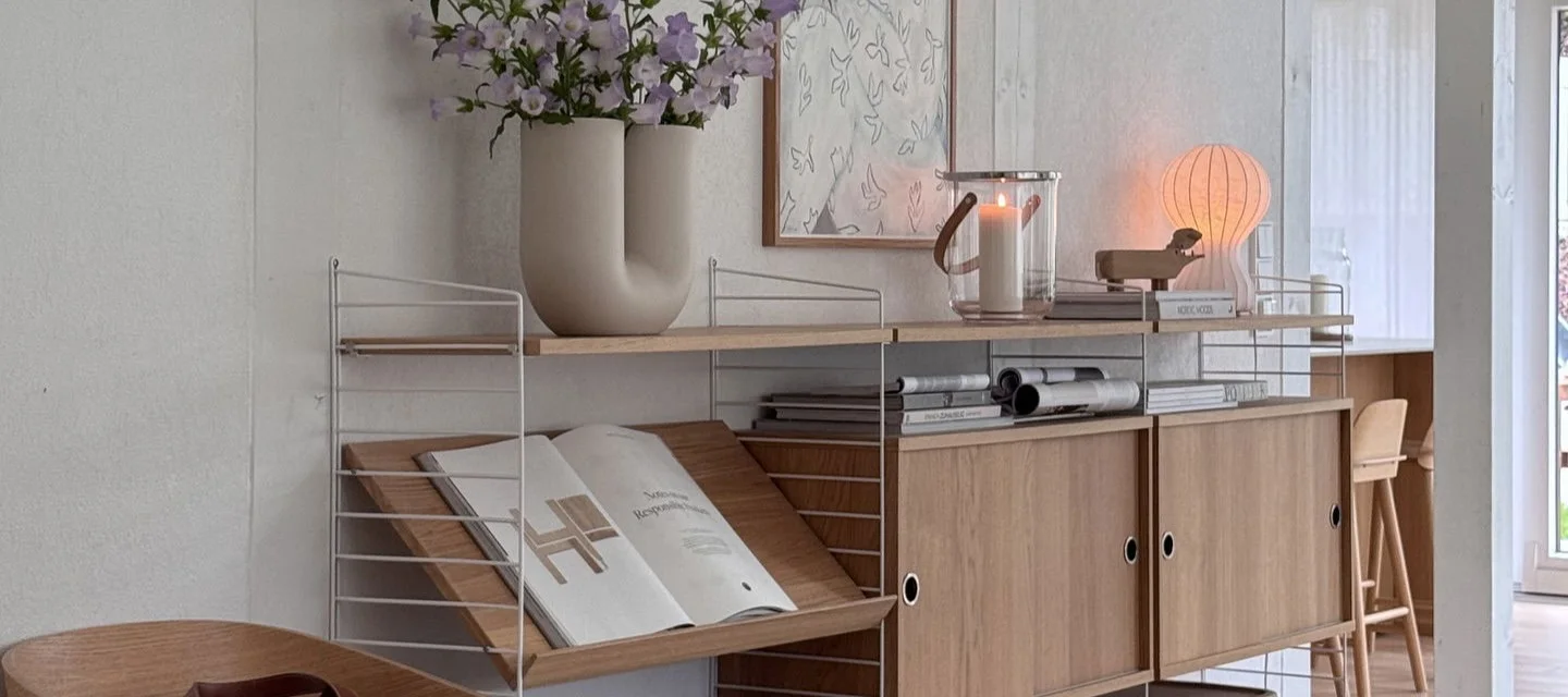 Modulair rekkensysteem: witte frames, houten planken, kasten, vaas met bloemen, lantaarn en paddestoellamp.