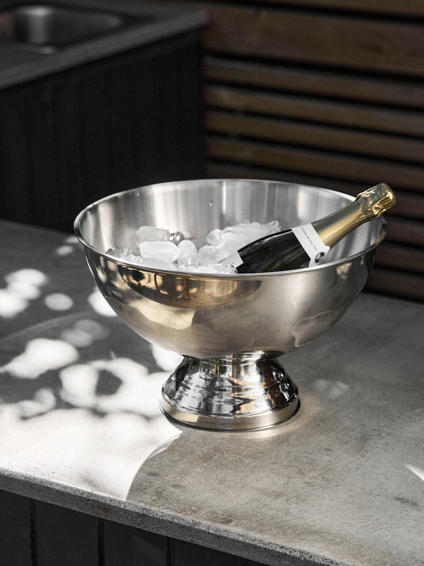 Champagnefles koelt in een roestvrijstalen ijsemmer op een betonnen oppervlak.