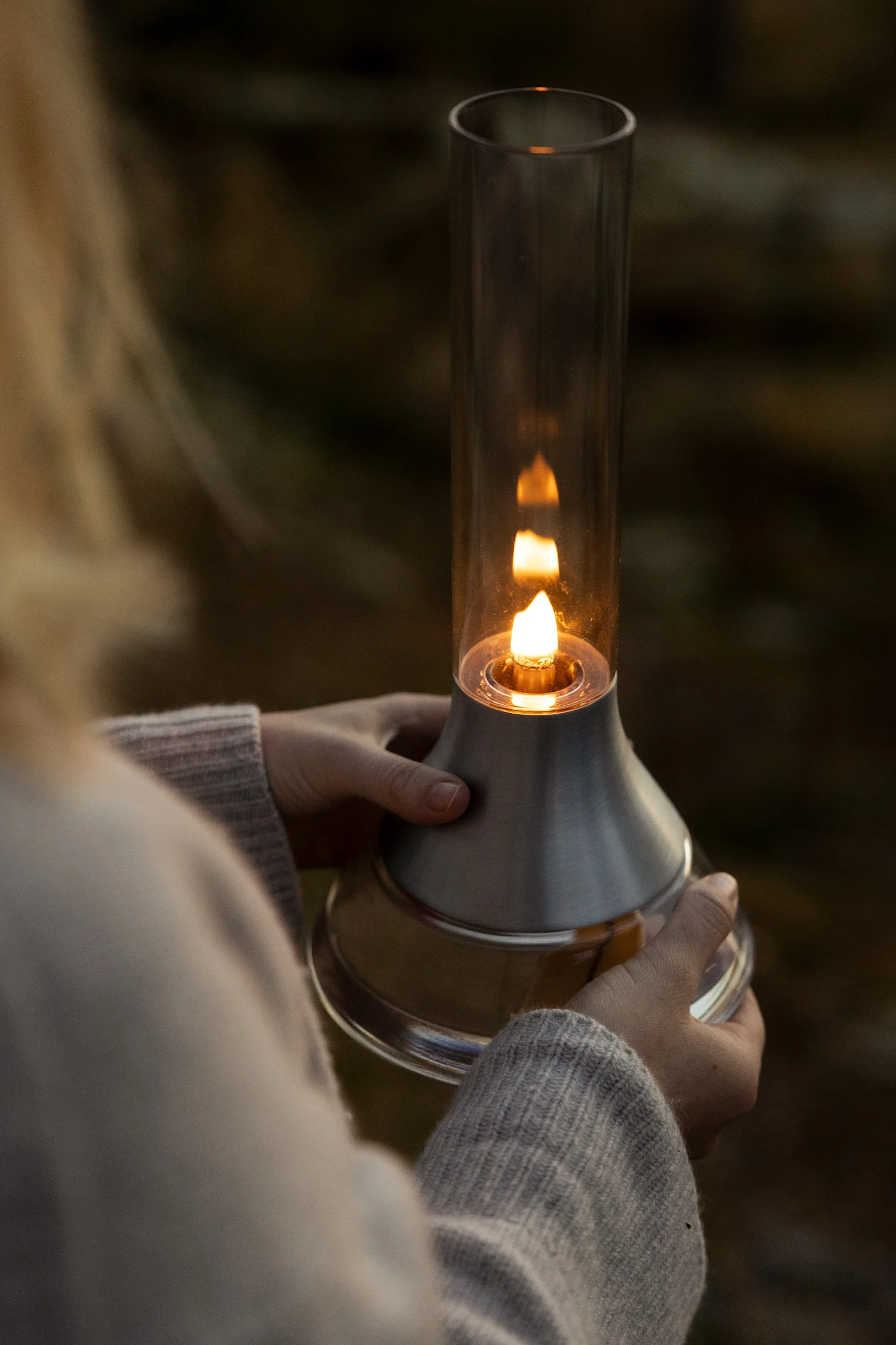 Persoon houdt een moderne lantaarn vast met een brandende vlam in een glazen cilinder en geborsteld metalen voet.