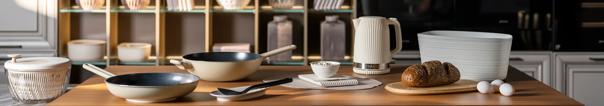 Keukenblad met beige koekenpannen, een witte geribbelde waterkoker, een brood met zaden op een plank en eieren. Moderne keukenaccessoires.