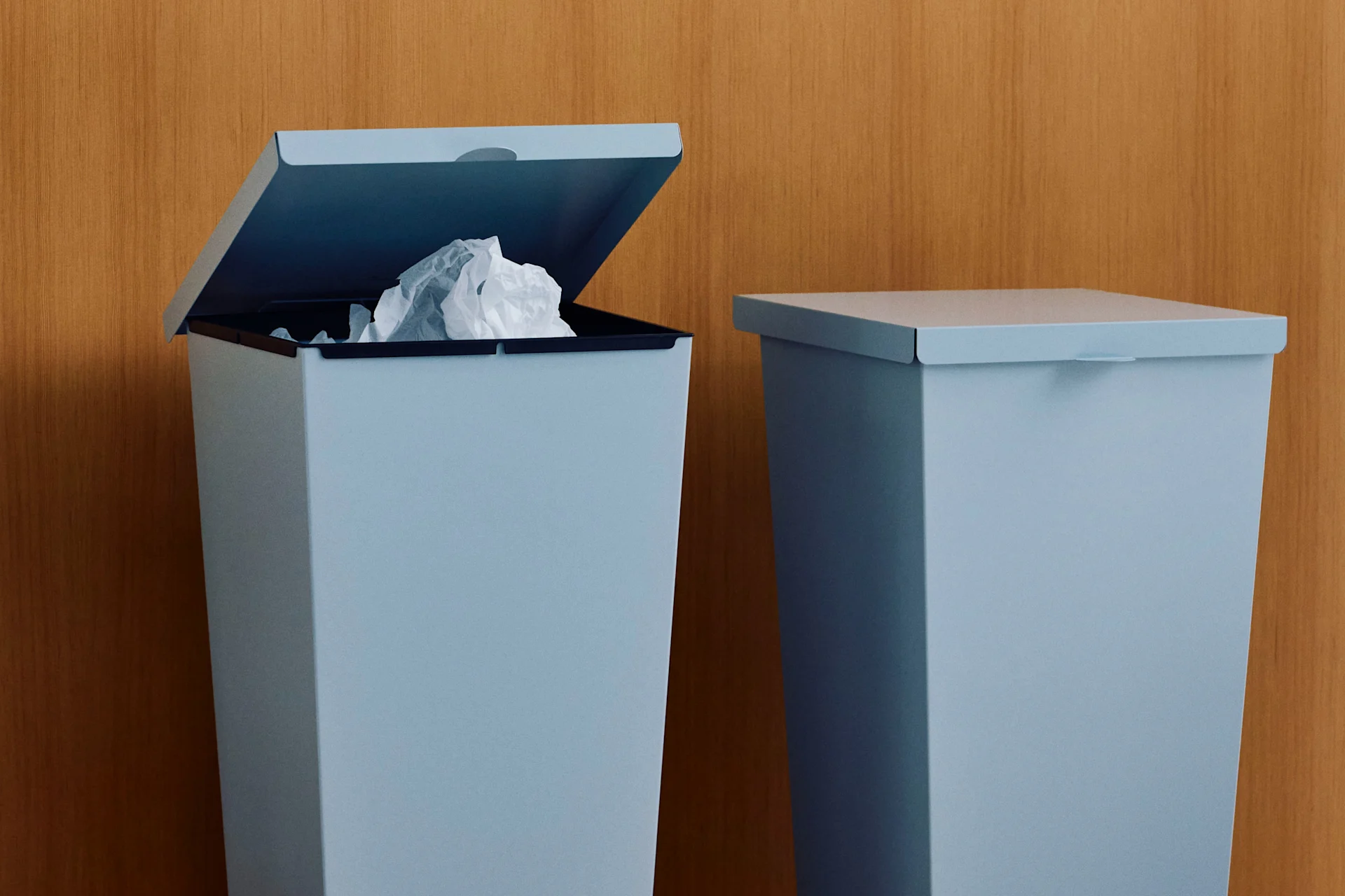 Twee lichtblauwe prullenbakken tegen een houten muur, één open met verfrommeld papier.