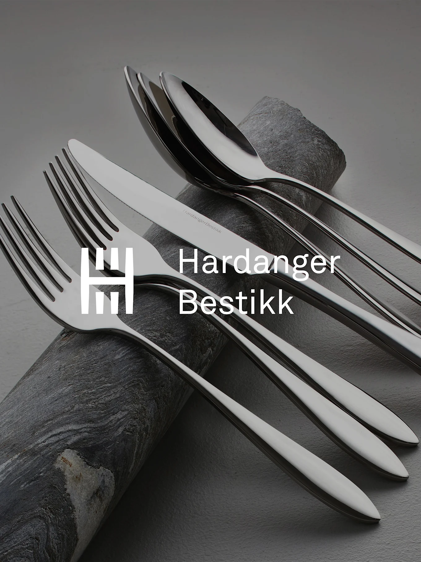 Glanzend roestvrijstalen bestekset, inclusief vorken, messen en lepels, kunstzinnig gerangschikt op donkere, getextureerde steen.