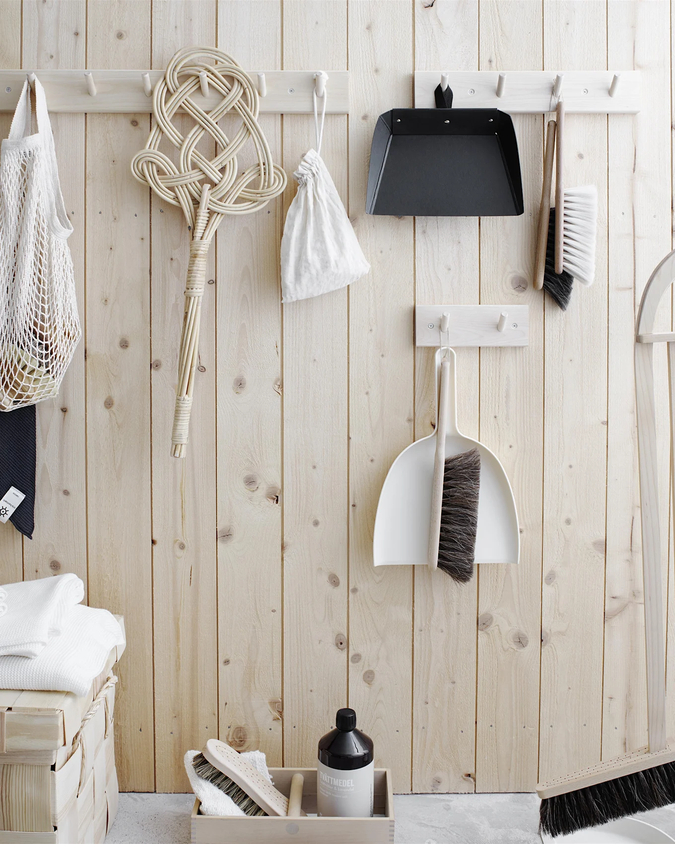 Schoonmaakgerei en wasbenodigdheden georganiseerd op een lichte houten muur. Inclusief borstels, stoffer en blik, een tapijtmepper, nettas, handdoeken en wasmiddel.