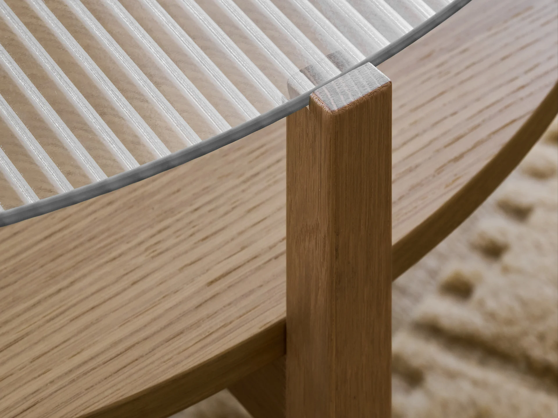 Close-up van een tafel met een geribbelde glazen blad en een lichtbruine houten poot.
