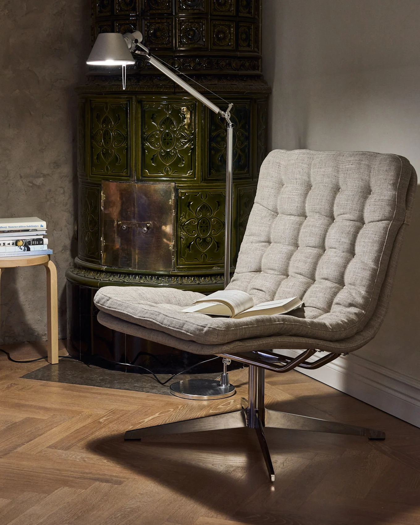 Gezellige leeshoek met een gecapitonneerde fauteuil, een verstelbare vloerlamp en een donkergroene tegelkachel.