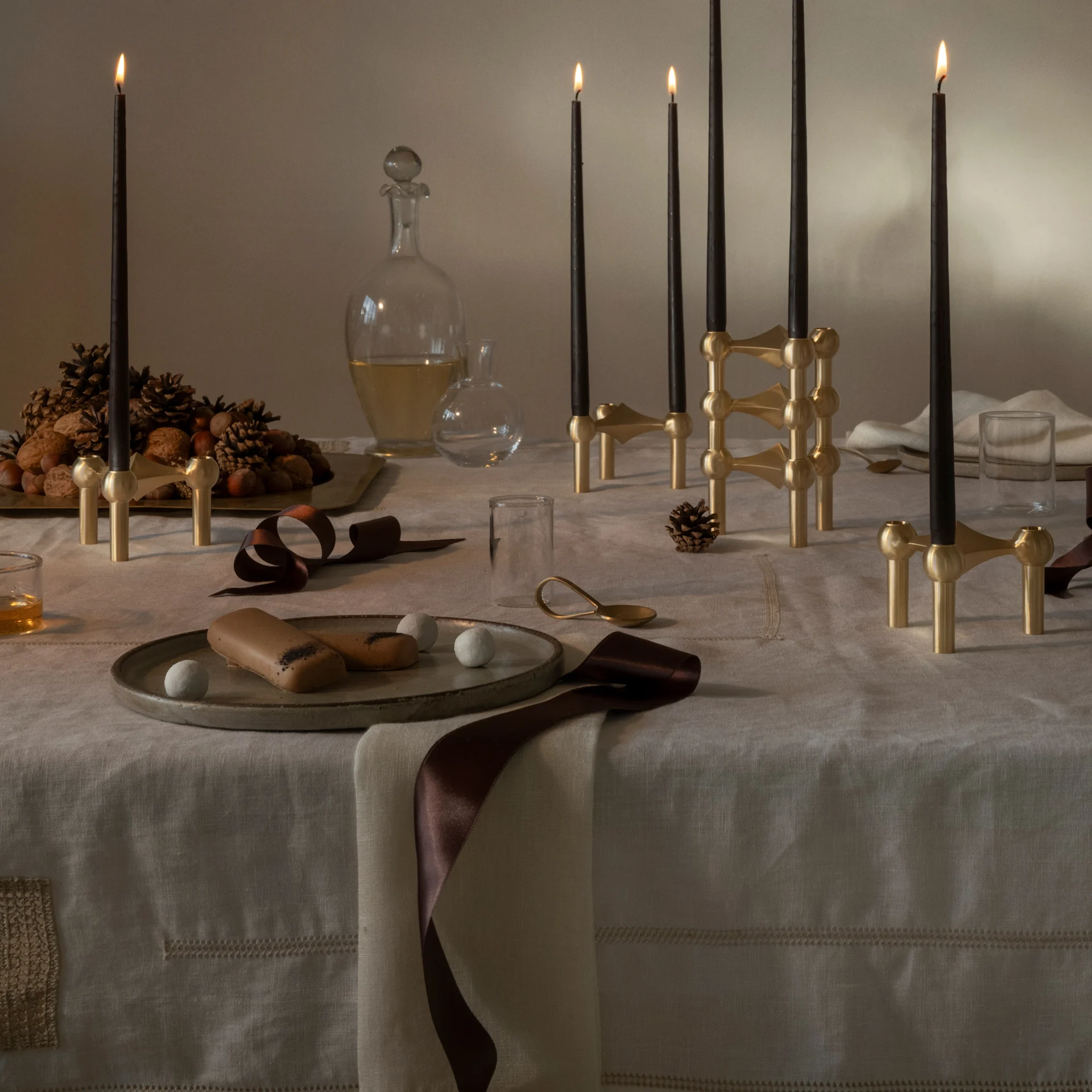 Feestelijk gedekte tafel: zwarte kaarsen in messing modulhouders, panettone, noten, dennenappels en desserts.