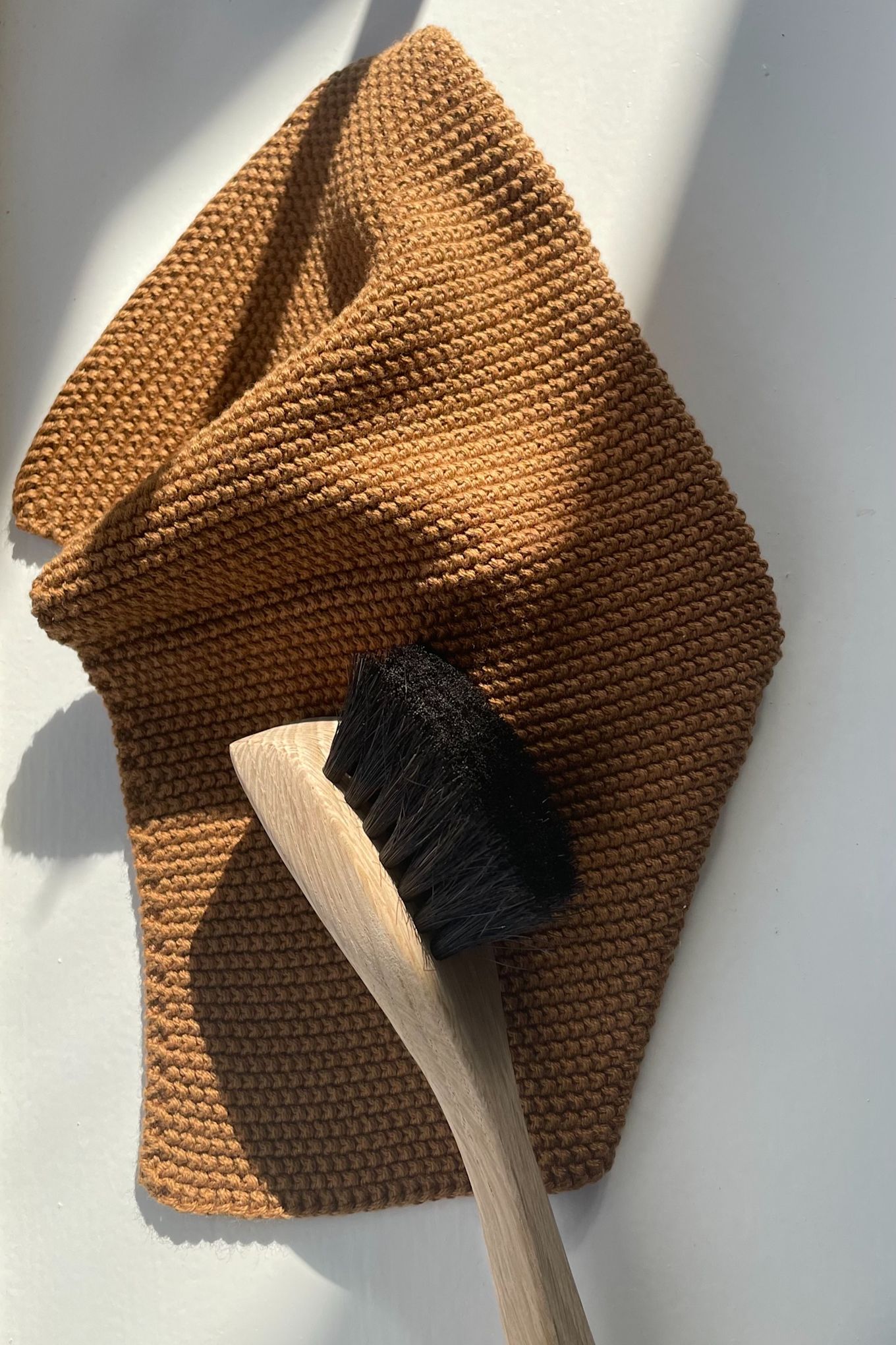 Maak je koekenpan schoon met een afwasborstel, hier afgebeeld op een bruine vaatdoek, beide van Humdakin.