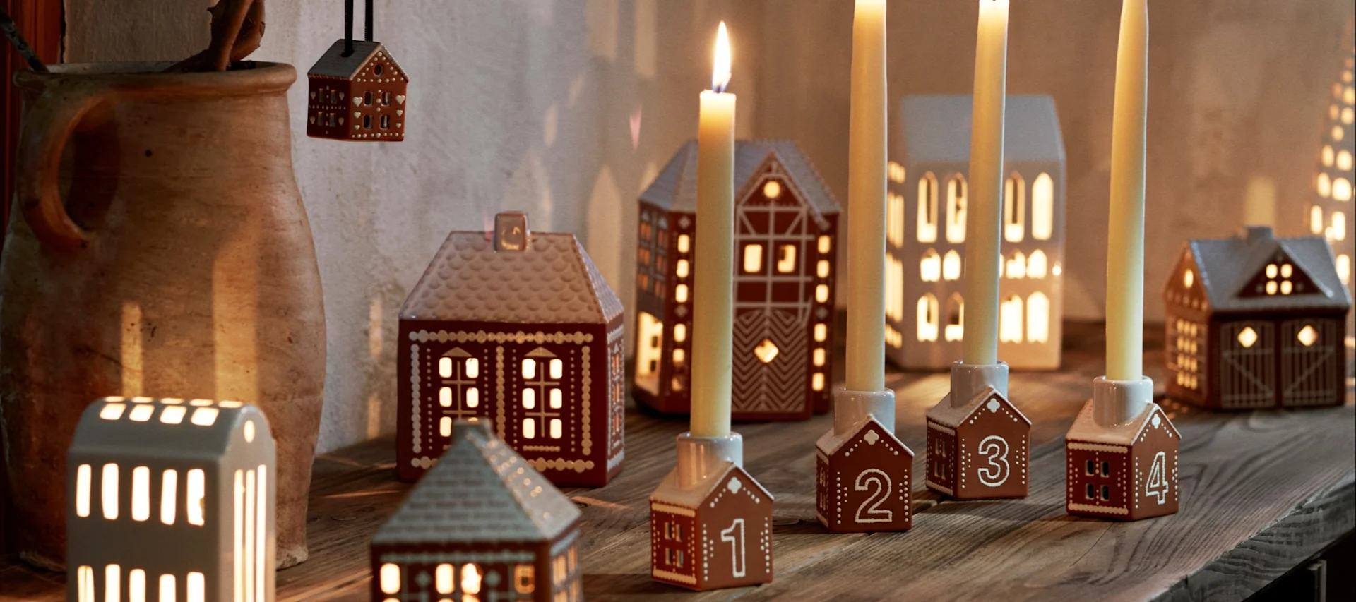 Decoreer met traditionele Scandinavische kerstdecoraties -  Hier zie je een jongetje dat een peperkoekhuisje eet op de vensterbank, omringd door andere kandelaars in de stijl van een peperkoekhuisje.