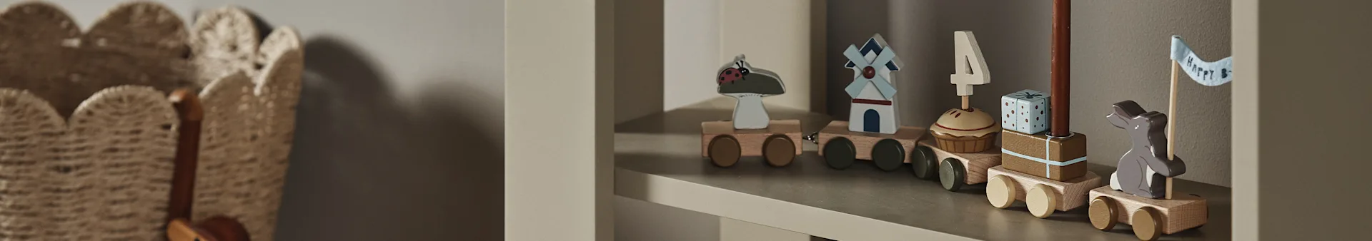 Een houten speelgoedtrein op een plank, met wagons met een lieveheersbeestje, windmolen, cupcake met '4' kaars, cadeau en een konijntje met een "Happy B" vlag.