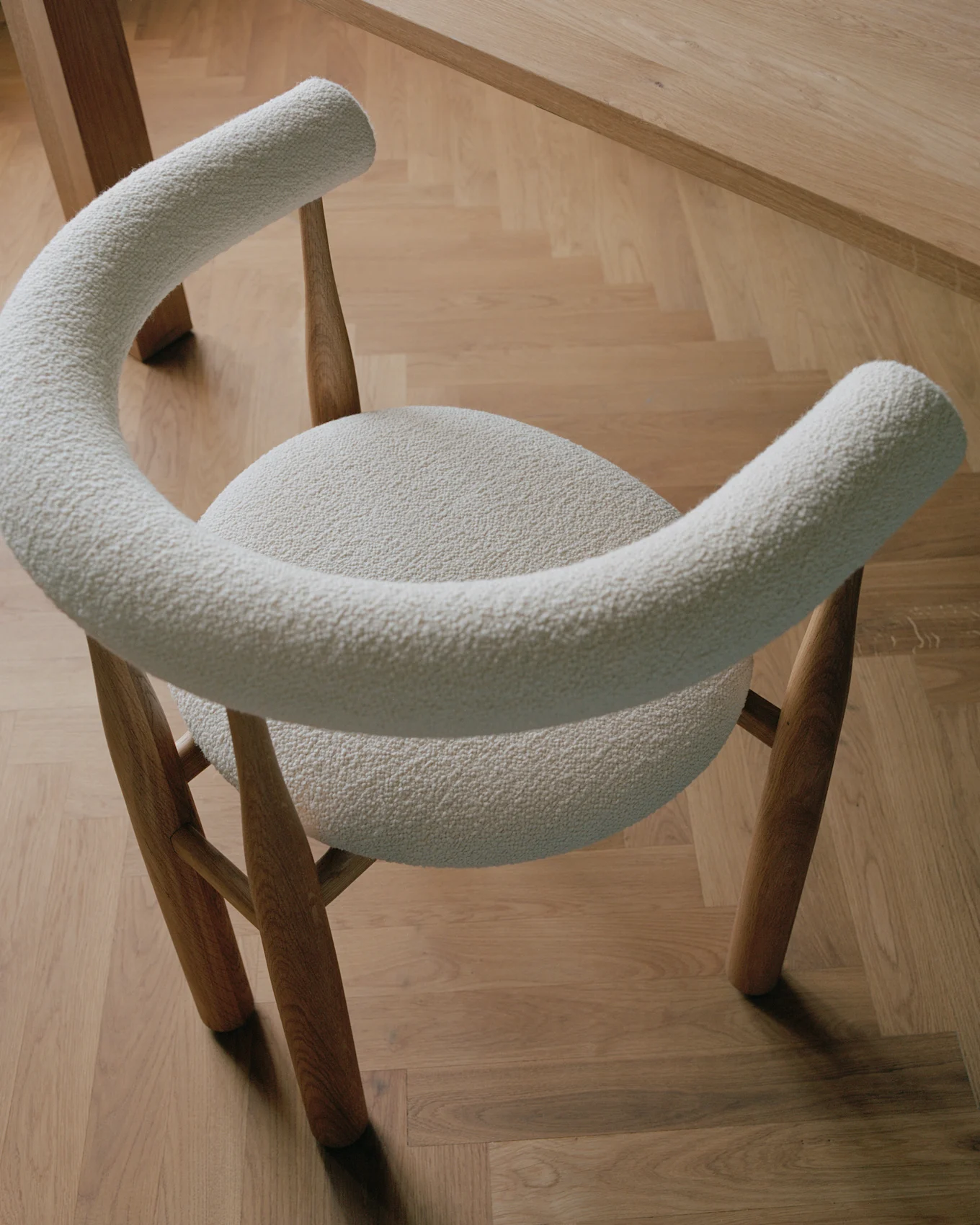 Moderne stoel met lichtcrèmekleurige bouclé-bekleding en houten poten, op een lichte houten parketvloer.