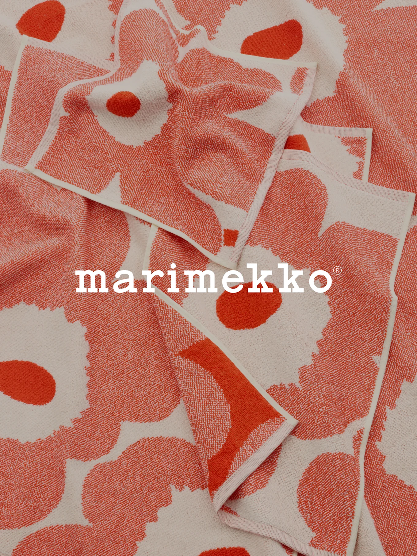 Gevouwen koraal- en gebroken witte handdoeken met patroon en Marimekko-logo.