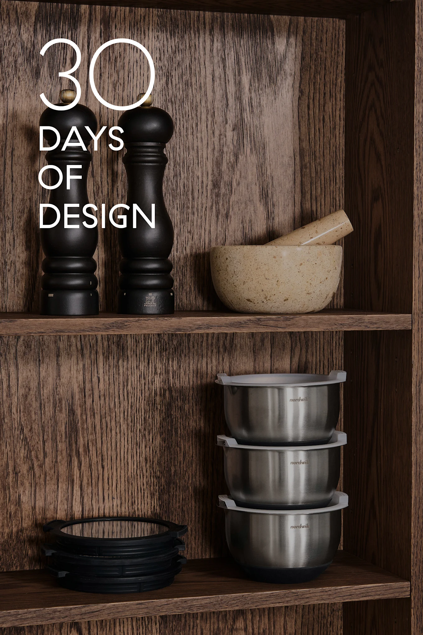Houten planken met keukengerei: zwarte molens, vijzel & stamper, stalen kommen, siliconen ringen. Tekst: 30 DAYS OF DESIGN.