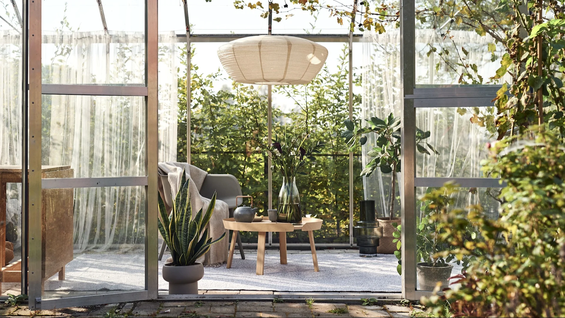 Vloerkleed voor buiten: Hier zie je een serre die is omgetoverd tot een gezellige woonkamer met een hanglamp, een stoel, een bijzettafel en een groot vloerkleed voor buiten.