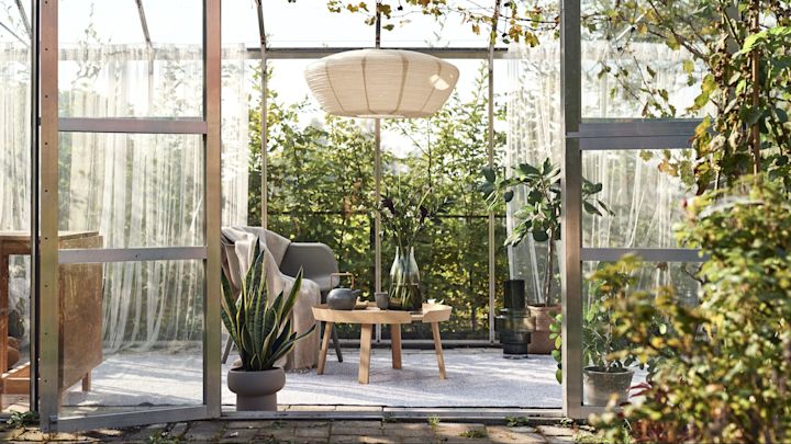 Vloerkleed voor buiten: Hier zie je een serre die is omgetoverd tot een gezellige woonkamer met een hanglamp, een stoel, een bijzettafel en een groot vloerkleed voor buiten.