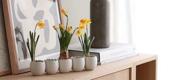 De Easter line paasdecoractie van Cooee Design is beplant met narcissen en staat op een houten commode.