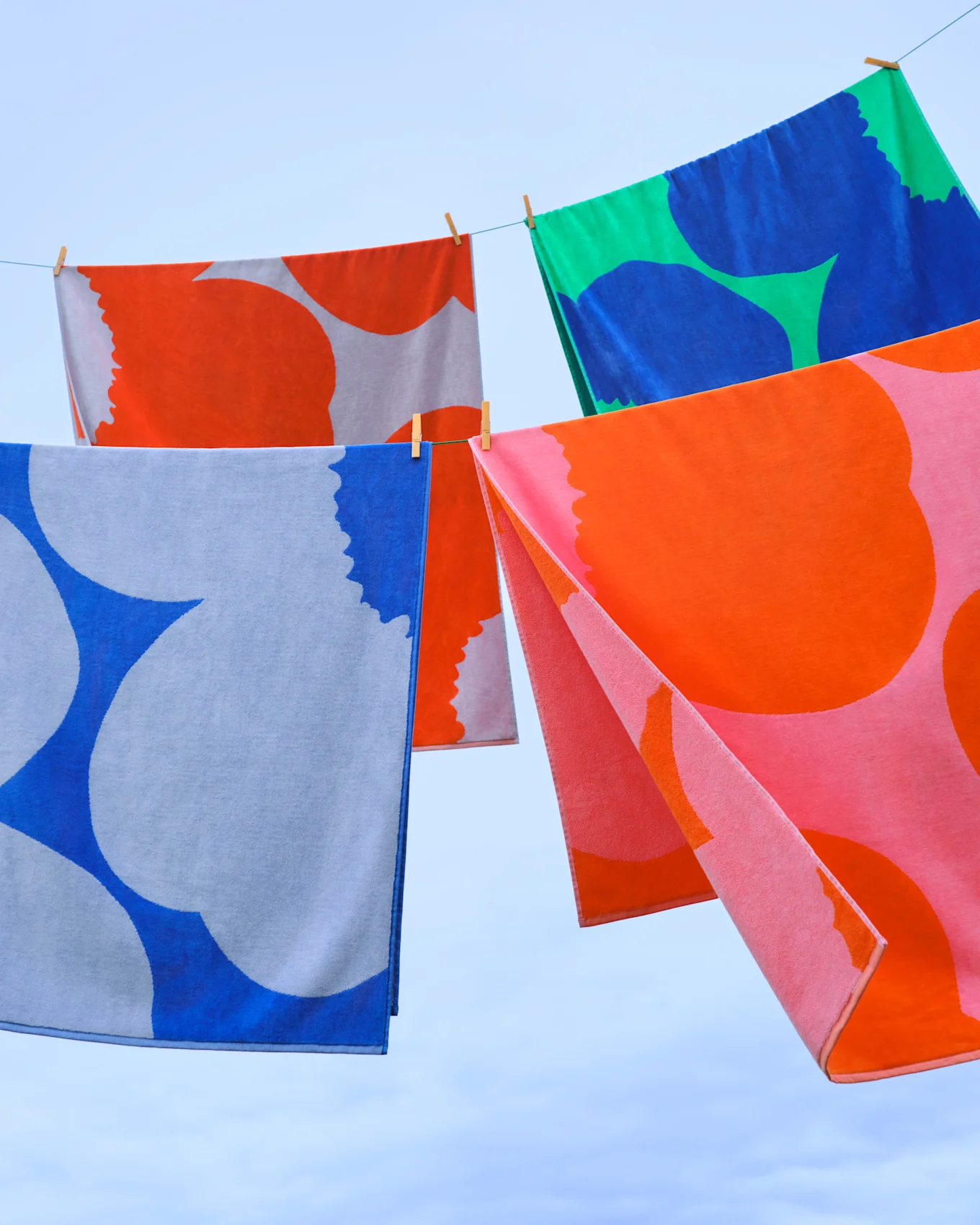 Kleurrijke handdoeken met patronen hangen aan een waslijn tegen een blauwe lucht.