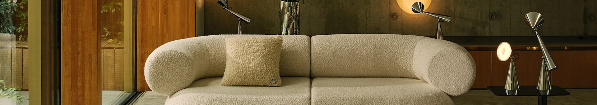 Moderne woonkamer met een gebroken wit bouclé modulair bankstel, een licht patroon vloerkleed en metalen lampen.