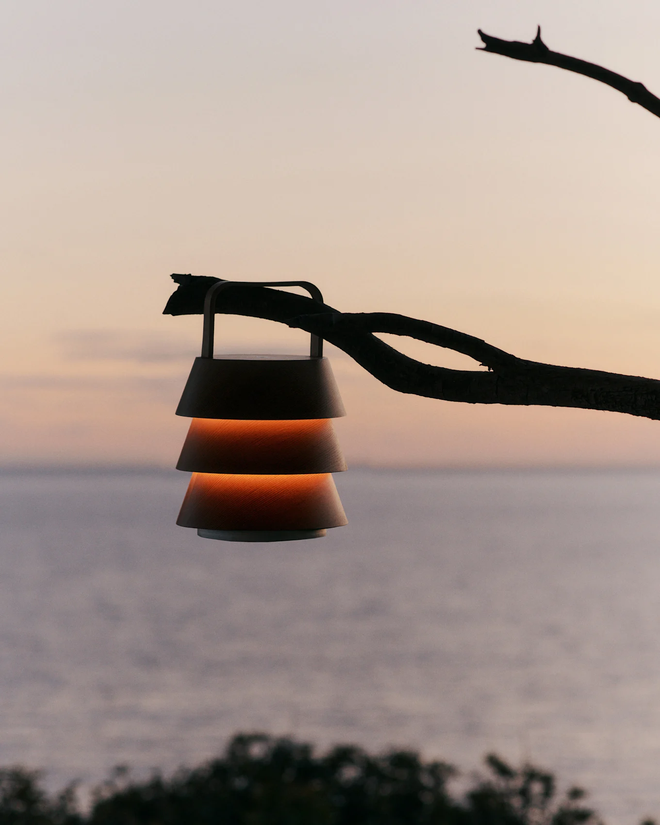 Lantaarn met gelaagde kappen hangend aan een tak tegen een zonsonderganglucht boven water.