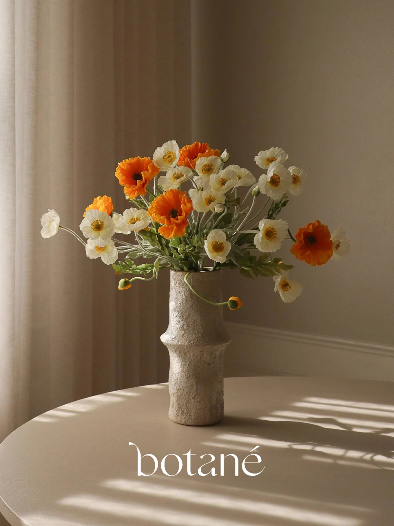 Een getextureerde vaas met een boeket oranje en witte kunstklaprozen op een tafel met gestreepte schaduwen.