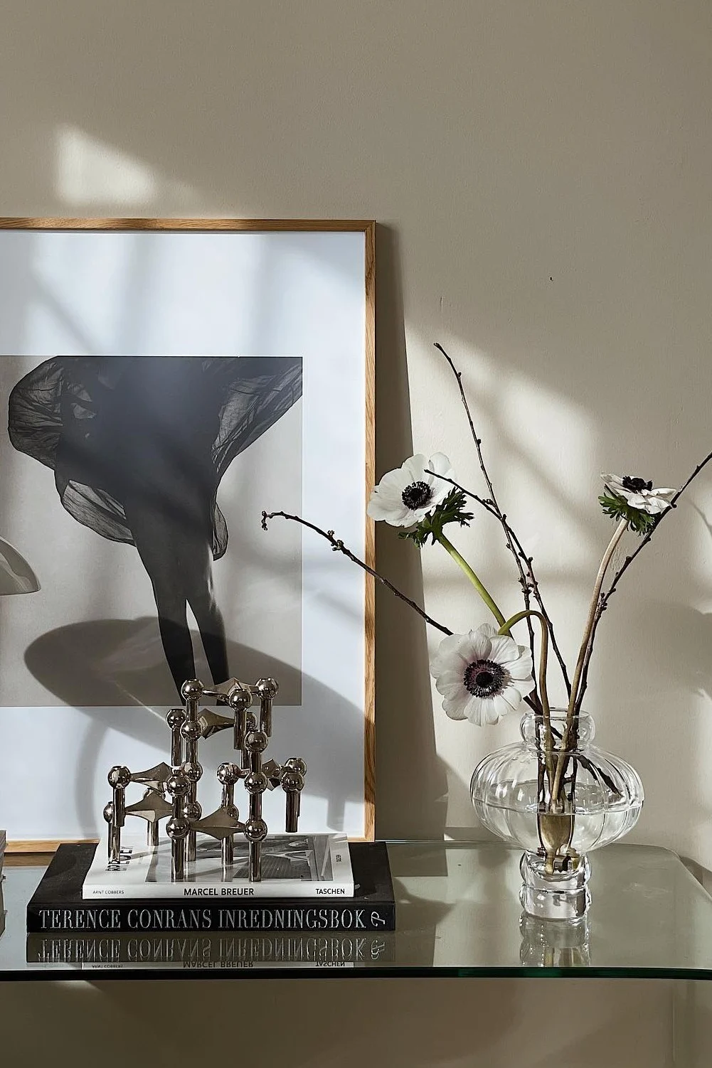 Ingelijste Z/W-foto van benen met wapperende stof, zilveren kandelaar, boeken en witte anemonen in vaas.