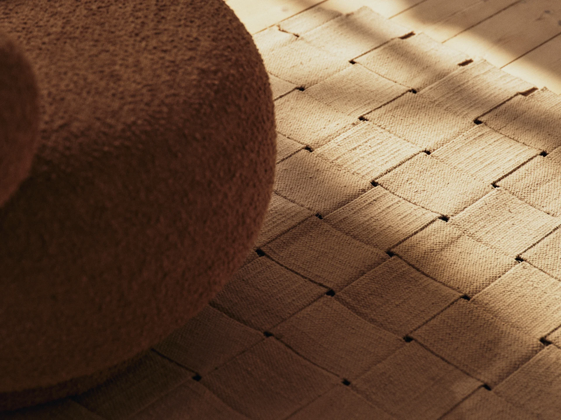 Bruine bouclé meubels, een geweven vloerkleed en een houten vloer met zonovergoten schaduwen.