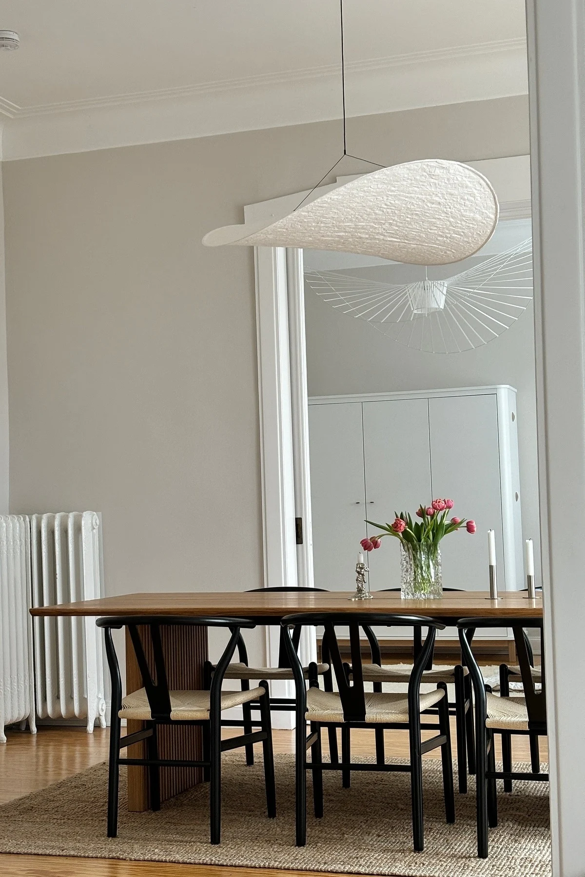 Moderne lampen transformeren je huis in een handomdraai. Hier zie je de Tense hangende plafondlamp van New Works boven een eettafel met een boeket tulpen. 