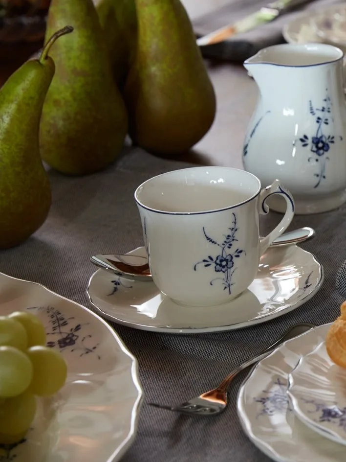 Wit porseleinen theekopje, schotel en schenkkan met blauw bloemmotief op een tafel met peren en druiven.
