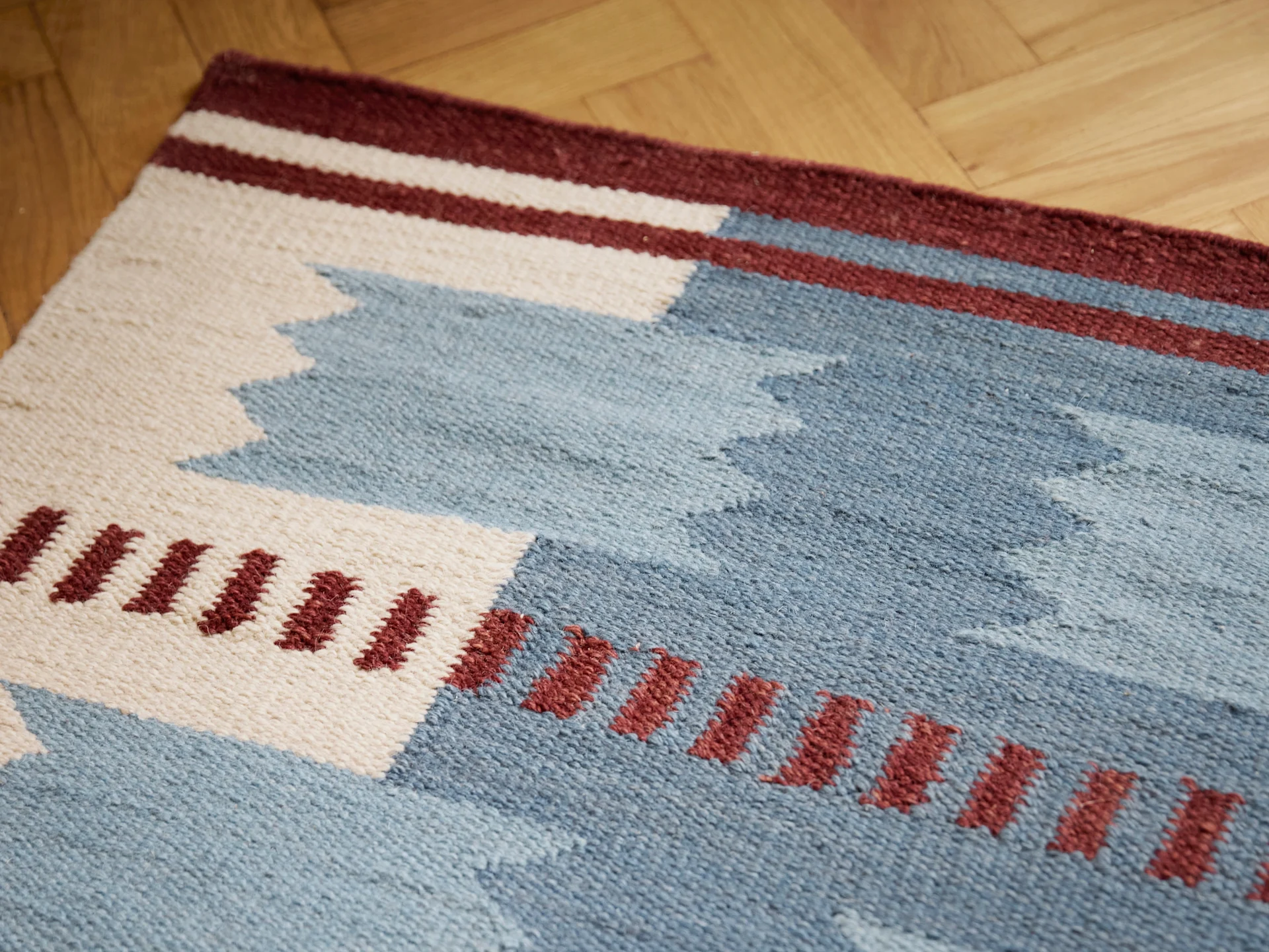 Geweven tapijt met geometrische patronen in blauw, wit en bordeaux op een houten vloer.