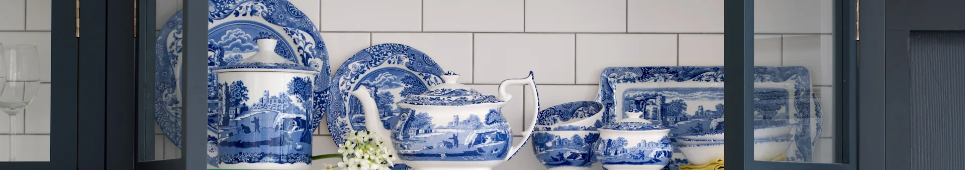 Blauw-wit gedecoreerd porseleinen servies met theepot, borden en schalen in een donkerblauwe kast.
