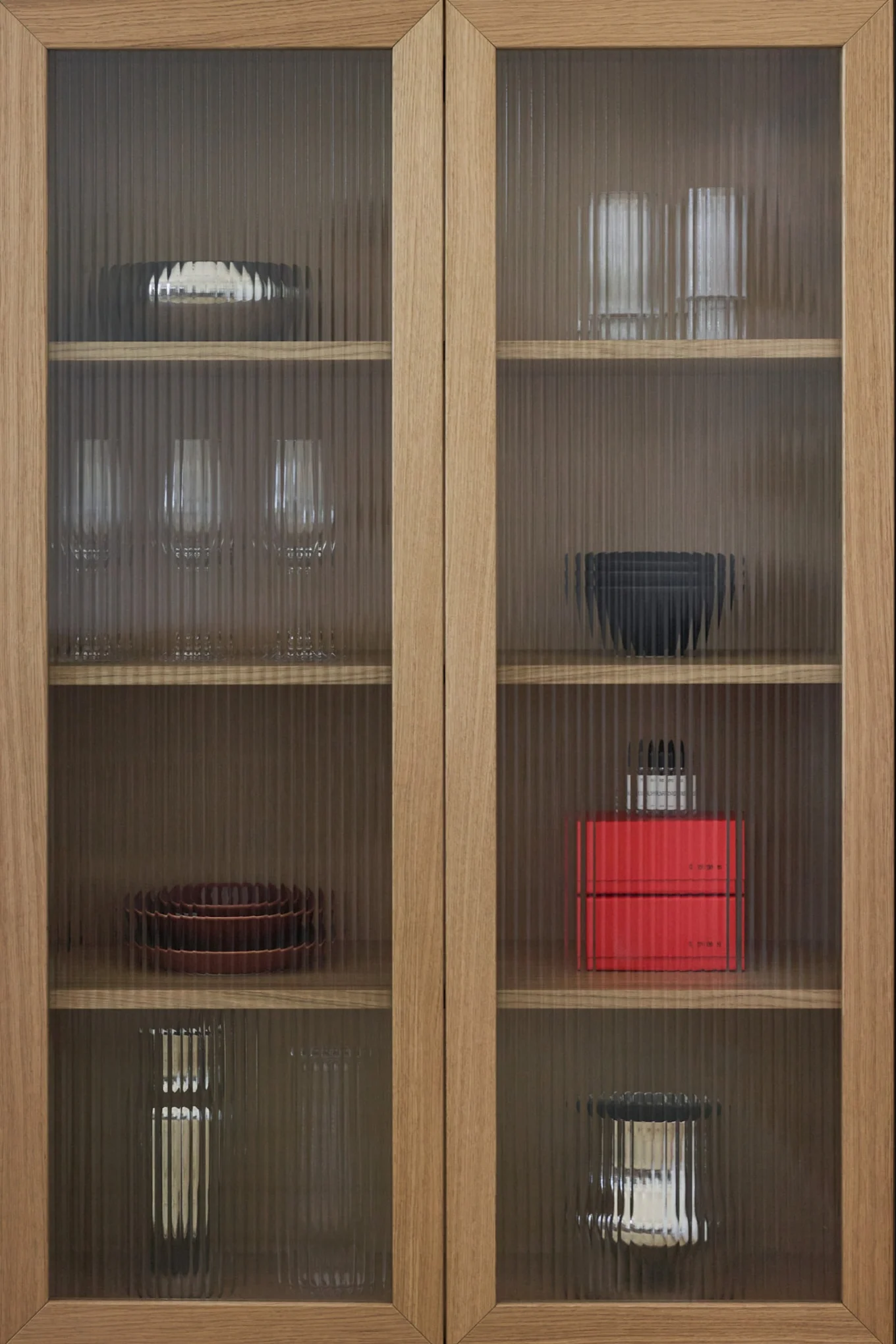 Houten kast met geribbelde glazen deuren, met diverse schalen, glazen en decoratieve voorwerpen op planken.