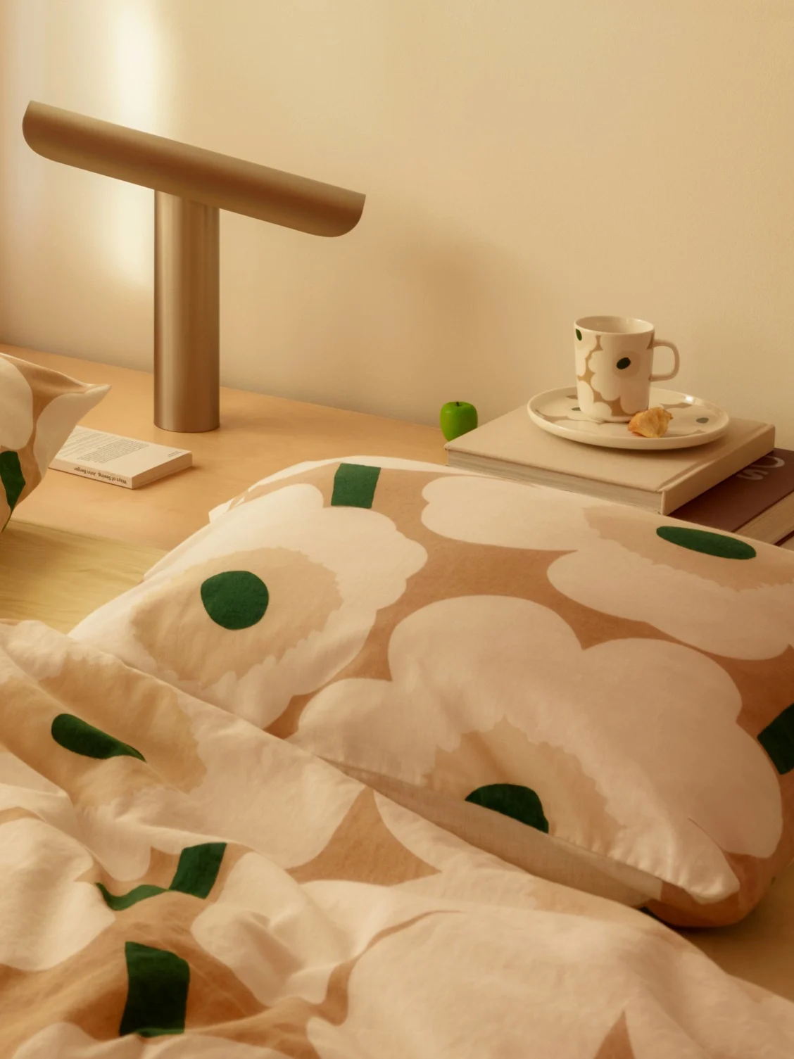 Bedtafereel met wit en beige bloemenbeddengoed, een moderne lamp, een kop en een boek op een houten nachtkastje.