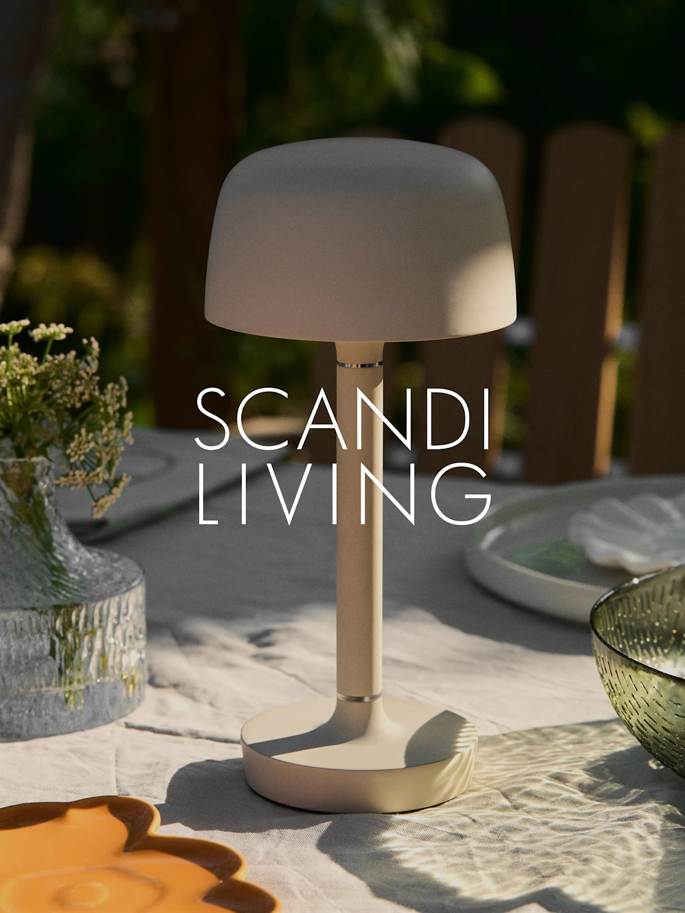 Een beige moderne draagbare tafellamp op een buitentafel met een vaas bloemen en servies. Tekst "SCANDI LIVING".