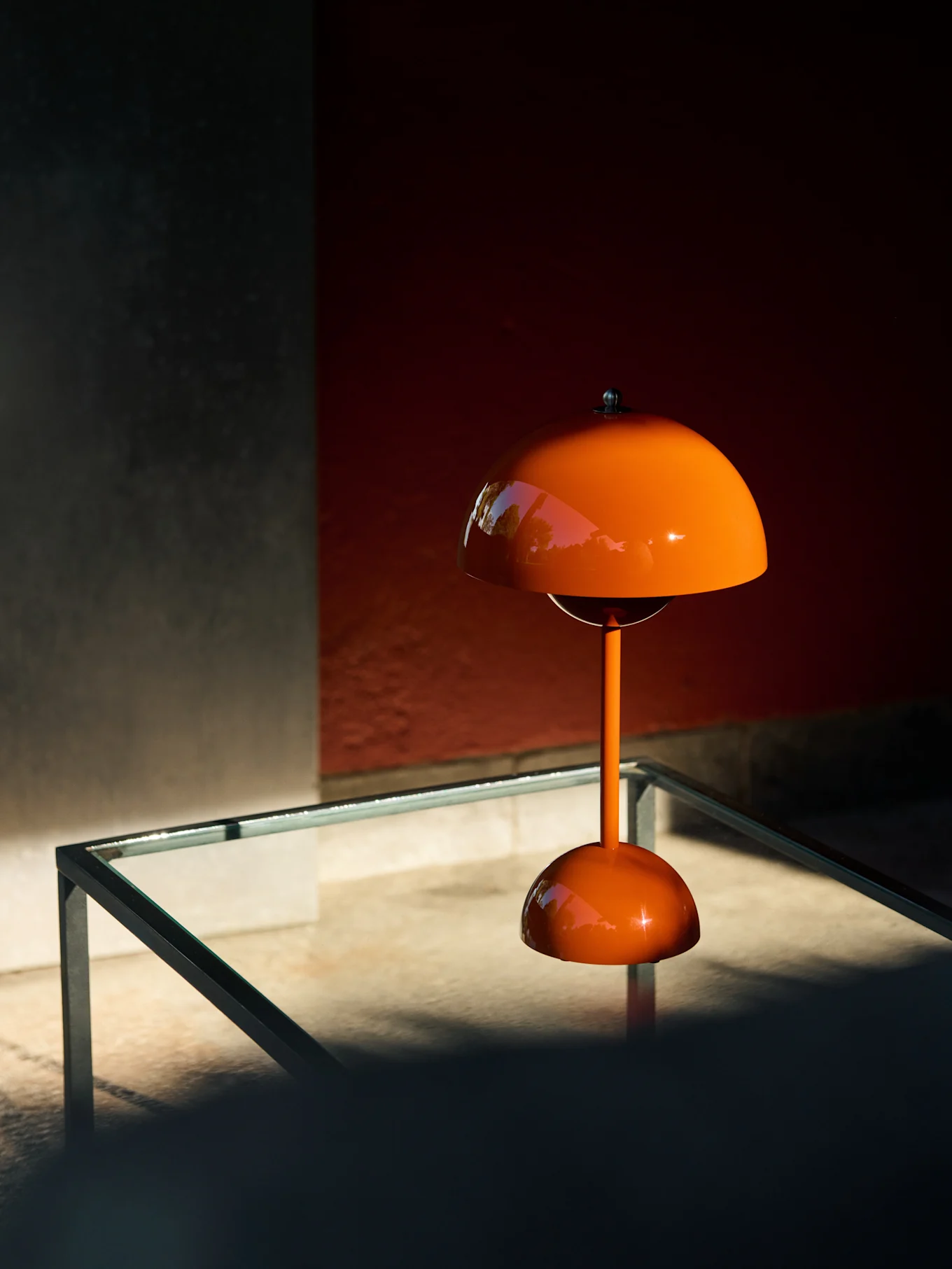 Oranje paddenstoelvormige tafellamp op een glazen tafel, met reflecties van groen.