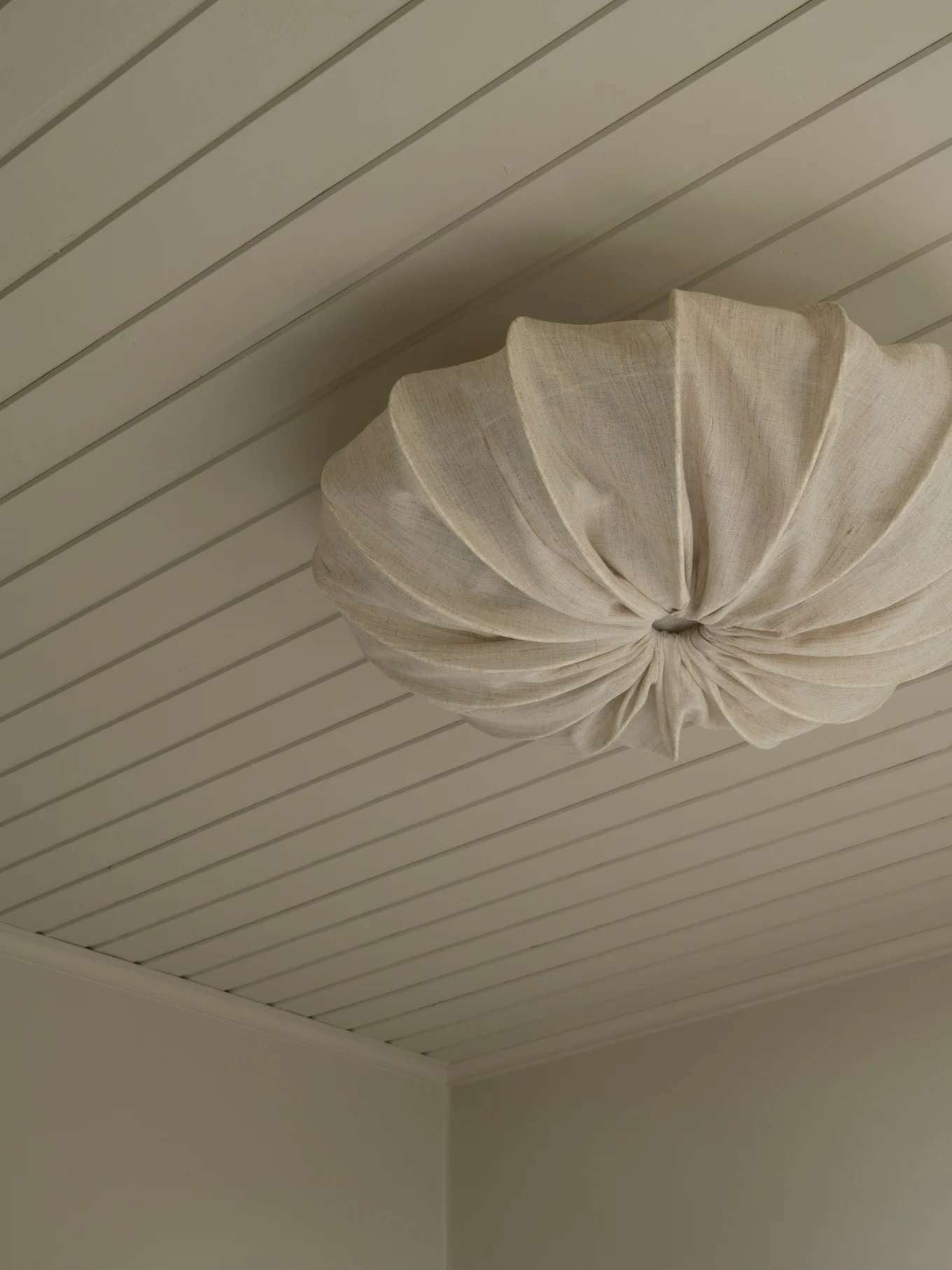 Een crèmekleurige geplooide stoffen plafondlamp gemonteerd aan een licht plafond met panelen.