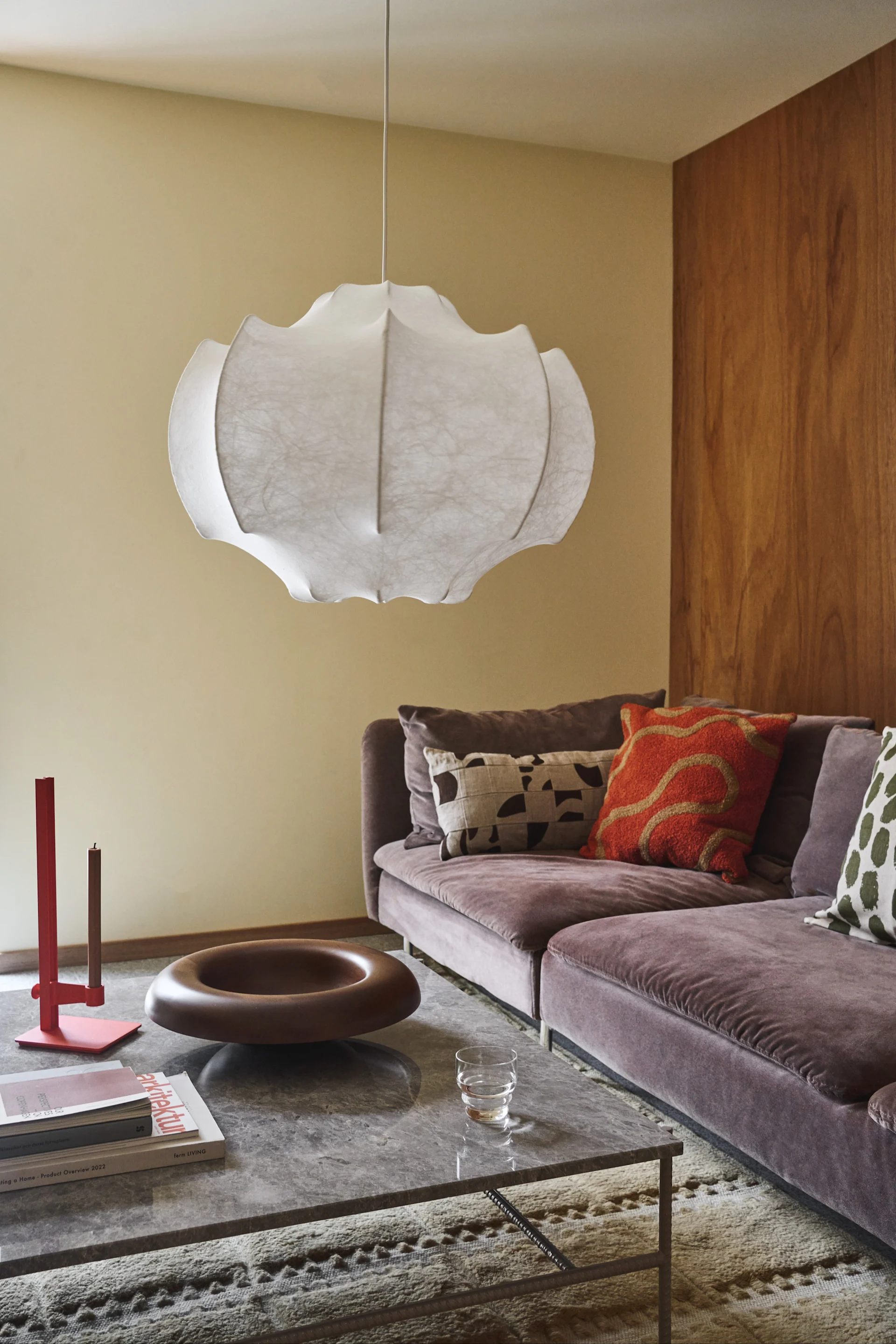 Moderne woonkamer met een grote witte hanglamp, een paarse fluwelen bank met kussens en een marmeren salontafel.