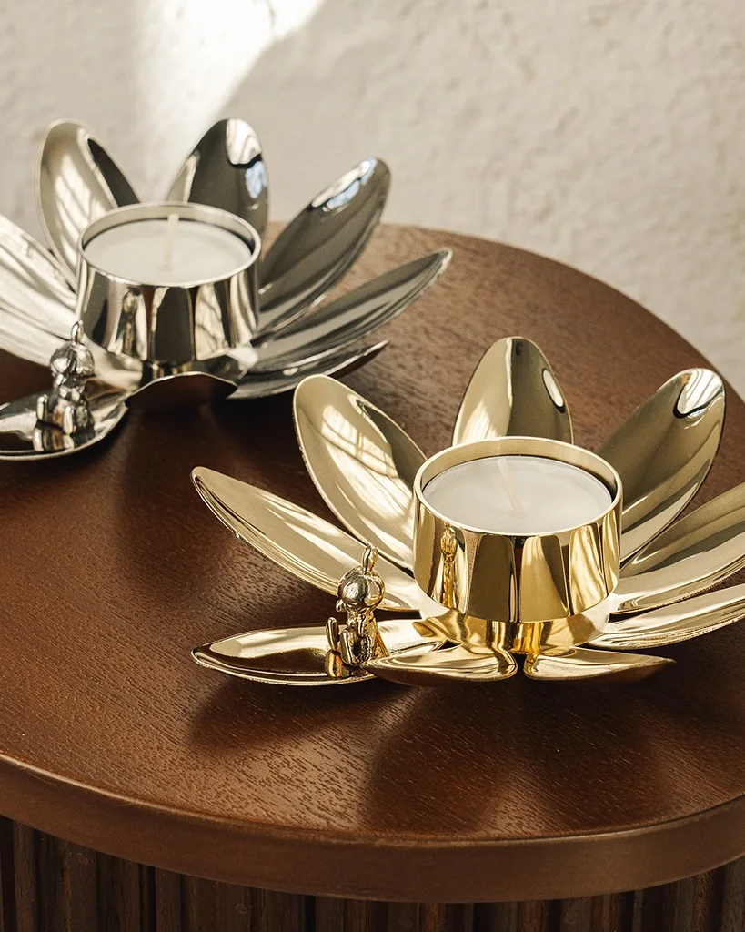 Twee lotusvormige theelichthouders, één zilver en één goud, met kleine Boeddha-beeldjes, op een houten tafel.