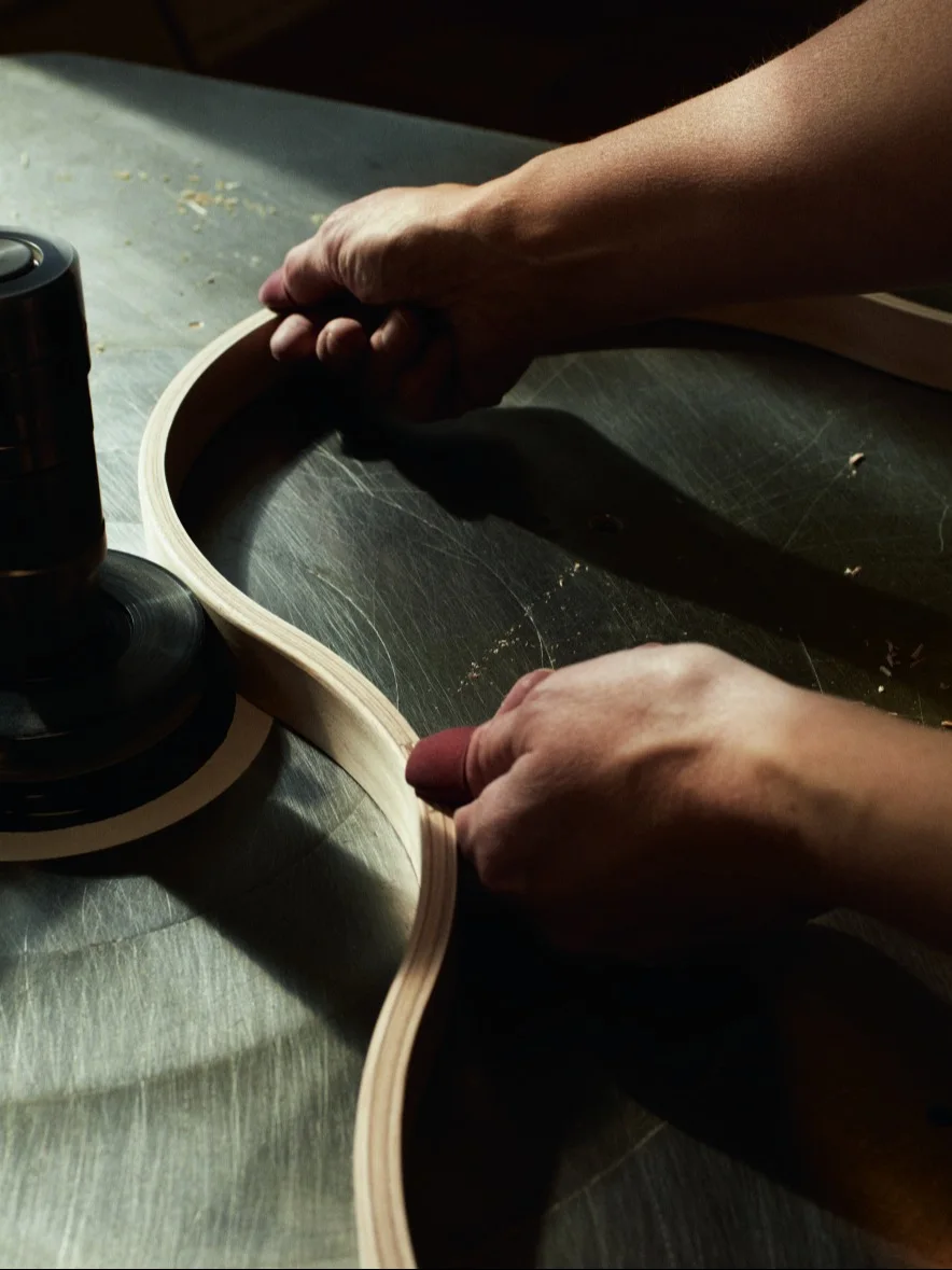 Handen schuren een gebogen houten strip op een werkplaatsmachine.