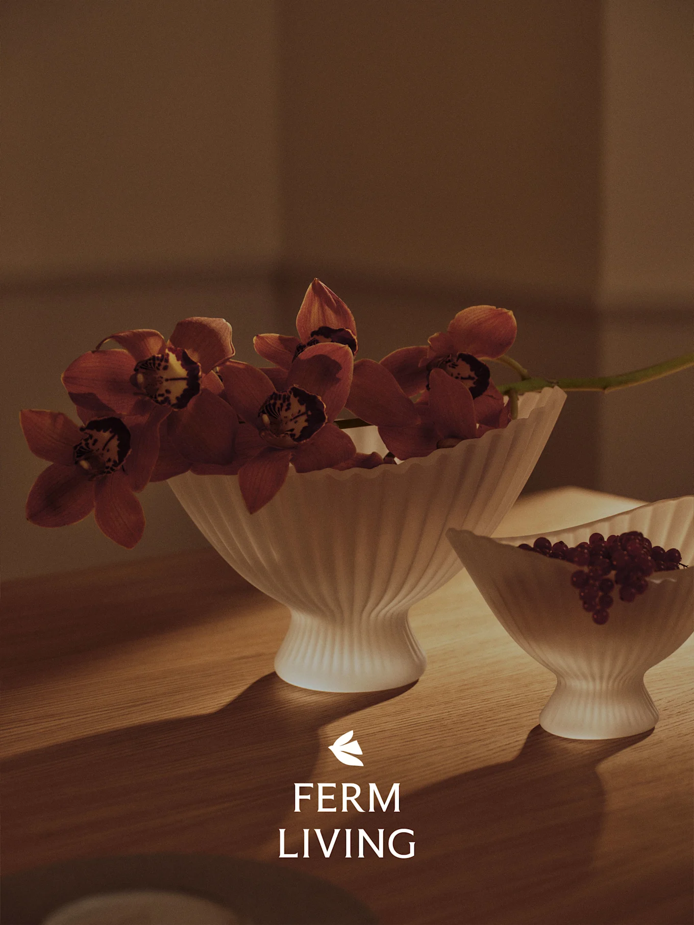 Twee geribbelde witte kommen op een houten tafel, de ene met rode orchideeën, de andere met rode bessen, in warm licht.