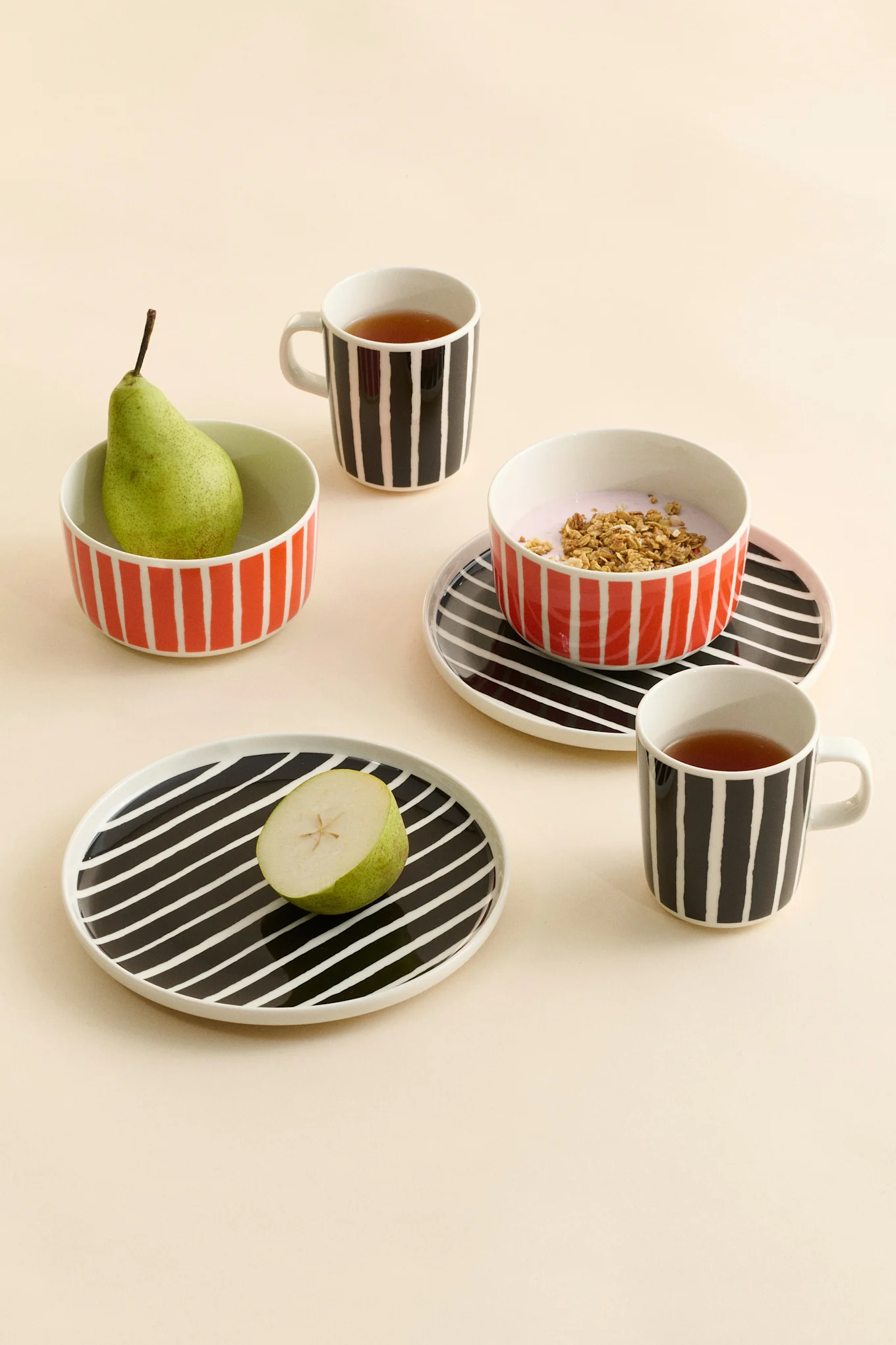 Gestripte keramische mokken met thee, kommen met een peer en yoghurt met granola, en borden met een halve peer.