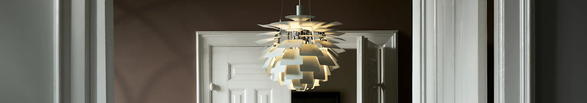 Een witte, sculpturale pendellamp met meerdere lagen verlicht een deuropening.