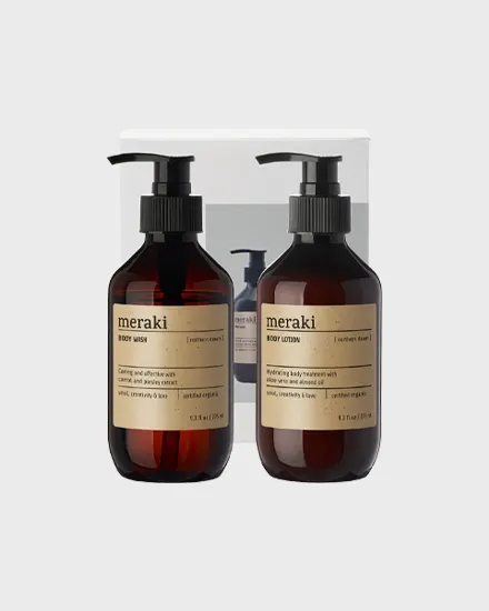 Twee donker amberkleurige Meraki-flessen met zwarte pompen, één body wash en één body lotion, op een lichtgrijze achtergrond.